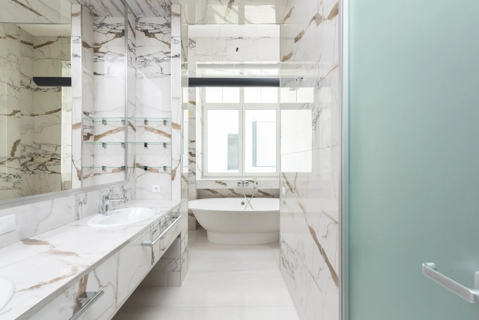 A bright marble bathroom with a white bath and basin.